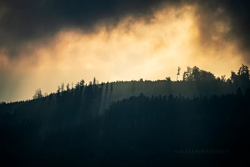 Haze and clouds forming around hilly forest during the sunrise